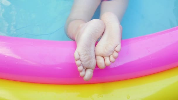 Crianças pés que põem na piscina inflável colorida do arco-íris. Rapariga de fato de banho cor-de-rosa a brincar na água num quintal. Verão relaxar, estilo de vida ativo, crianças nadar diversão lazer em casa, tempo quente 4K
 - Filmagem, Vídeo