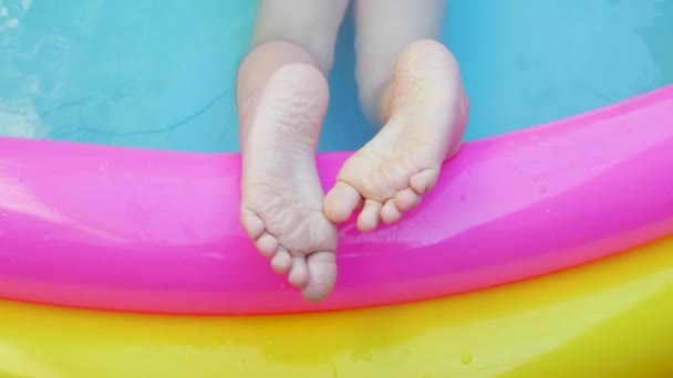Dzieci kładą stopy na kolorowym tęczowym, nadmuchiwanym basenie. Młoda dziewczyna w różowym stroju kąpielowym bawiąca się w wodzie na podwórku. Letni relaks, aktywny tryb życia, dzieci pływają zabawy w domu rekreacji, gorąca pogoda 4K - Materiał filmowy, wideo