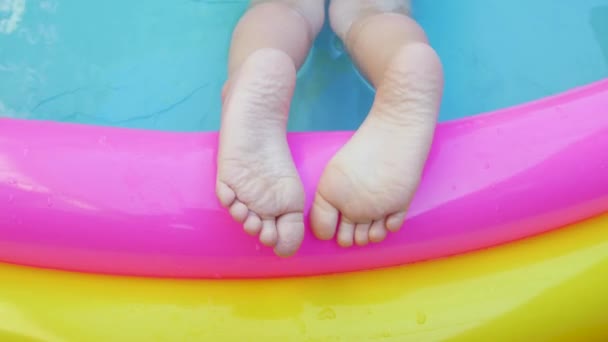 Kids feet laying on colorful rainbow inflatable swimming pool. Young girl in pink swimsuit playing in water on a backyard. Summer relax, active lifestyle, children swim fun home leisure,hot weather 4K - Footage, Video