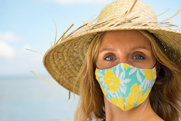 Funny portrait of young woman in straw hat on tropical sea beach. New rules to wear cloth face covering mask at public places due coronavirus COVID 19. Family holiday with kids, travel at summer 2020. - Photo, Image