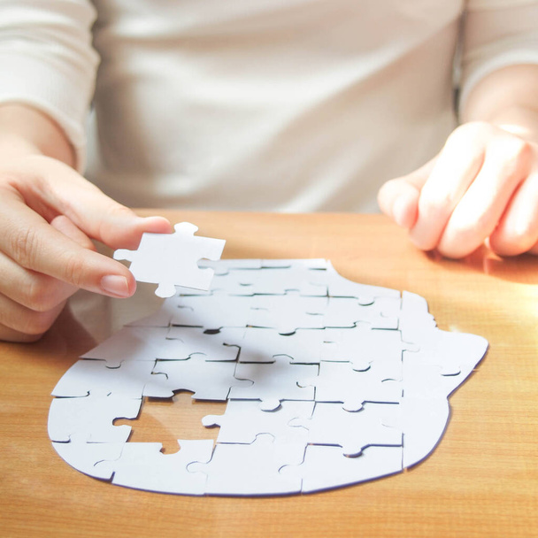 Female hands holding missing white jigsaw puzzle piece down into the place as a human head brain shape. Creative idea for memory loss, dementia, Alzheimer's disease and mental health concept. Square. - Photo, Image