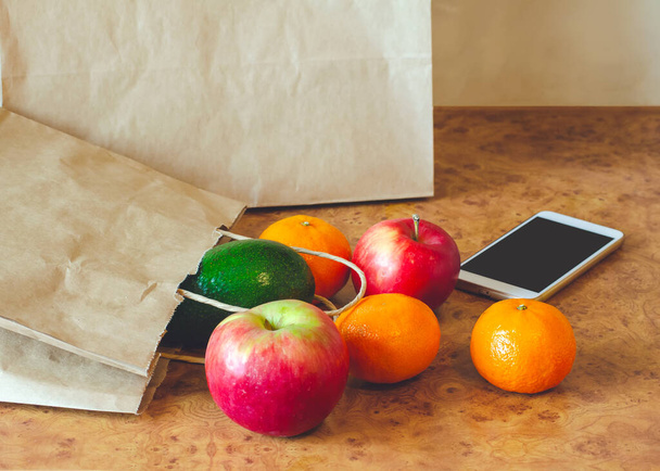 Bolsa de papel, diferentes frutas frescas, verduras y teléfono móvil sobre fondo de madera
. - Foto, Imagen