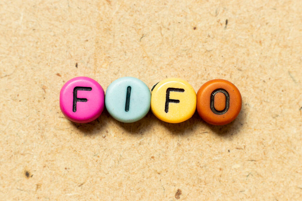 Круглая цветная бусинка с черной буквой в слове FIFO (аббревиатура "first in first out") на фоне дерева
 - Фото, изображение