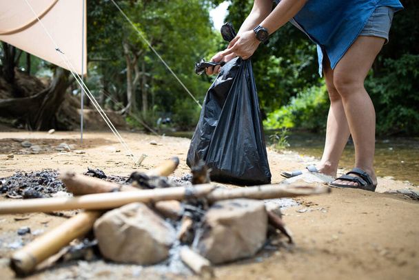 Asiáticos recogiendo basura con bolsa de basura en el parque nacional, turista recoger basura después de acampar en el bosque natural, tienda y arroyo en el fondo, el cuidado del medio ambiente, la protección de la ecología
 - Foto, Imagen