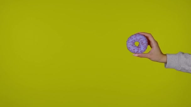 Vrouwelijke hand houdt een blauwe smakelijke en verse donut, gele achtergrond - Video