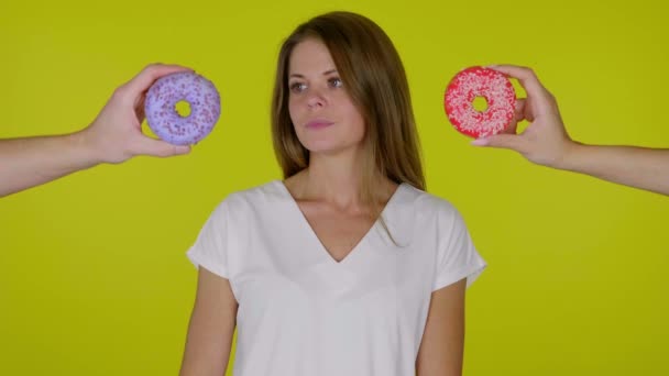 Confused woman in a white T-shirt looks around, cannot decide which donut to eat - Footage, Video