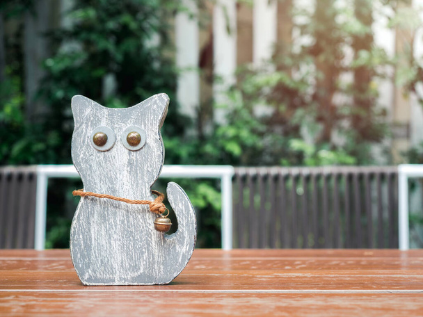 Linda muñeca de madera de gato con grandes ojos y campana en la mesa de madera sobre fondo de arbusto verde
. - Foto, Imagen