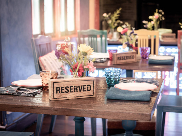 Panneau réservé en bois debout avec pot en verre et fleur sur la table à manger dans un restaurant de style rétro. - Photo, image