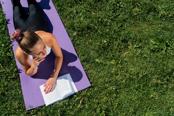 A brooding young girl with a book view from above, a sporty woman lies on a yoga mat on a summer day - Фото, зображення