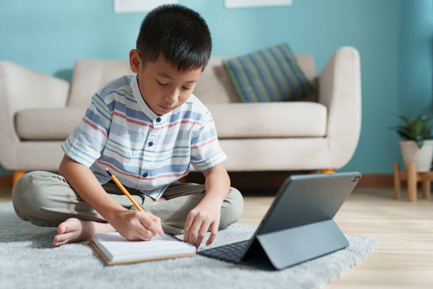 Education. Asian boy learning and doing homework with the online teacher on tablet digital at home - 写真・画像