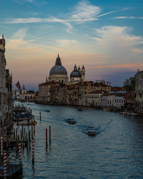 Vista desde el puente de la Academia en Venecia al atardecer, con canal, barcos y basílica. Cielo claro con bonitos colores y nubes
. - Foto, Imagen