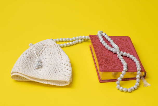 Pink Quran and white muslim rosary and white skullcap on a yellow background - Fotó, kép