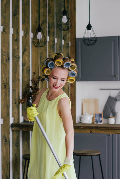 The girl in hair curlers washes floors in the kitchen mop - Фото, изображение