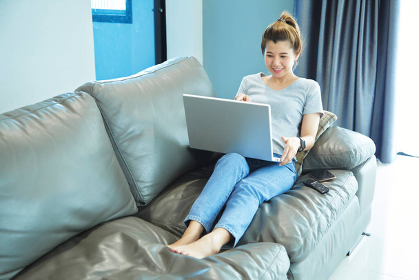 Женщина азиатка сидит на диване, используя ноутбук дома. Работа на дому
 - Фото, изображение