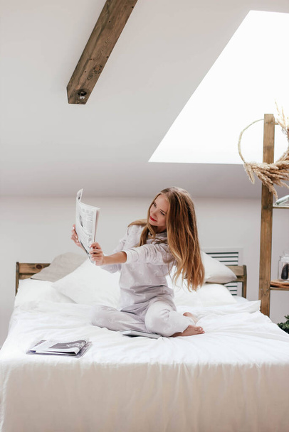 Blonde girl in white pajamas on the bed - Fotó, kép