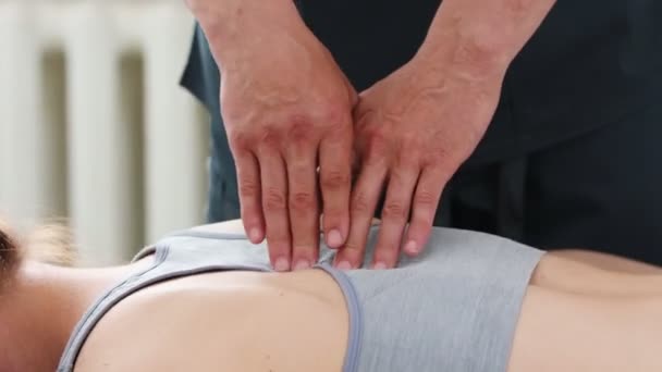 Jeune femme allongée sur un canapé à la clinique et le masseur appuyant sur sa colonne vertébrale avec ses doigts - Séquence, vidéo