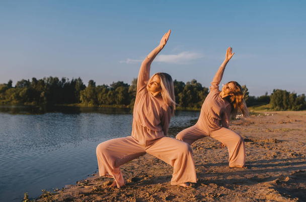 Due giovani donne che fanno esercizi di yoga sulla spiaggia all'alba. Bene sano. Rilassati vitale. Concetto sano - Foto, immagini
