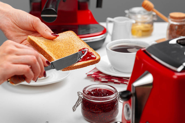 Female hand spresding strawberry jam on baked toast - Foto, Imagem