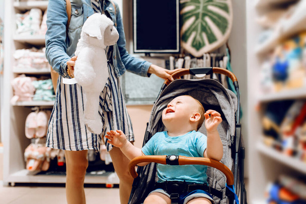 young beautiful woman in a medical protective mask on her face, with a small child in a stroller, shopping at a shopping center. Quarantine, coronavirus, shopping - 写真・画像