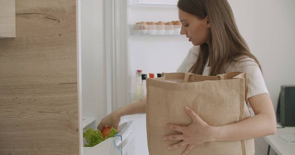 Young woman unpacking food bag into fridge - Foto, afbeelding