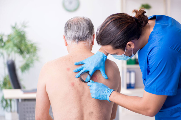 Oude man op bezoek bij jonge mannelijke arts dermatoloog - Foto, afbeelding