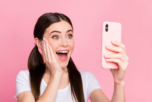 Closeup photo of pretty cheerful lady hold telephone hands excited emotions read positive comments arm on cheek wear casual white t-shirt isolated pastel pink color background - Fotó, kép
