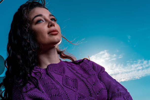 Attractive Woman With Curly Hair at Blue Bright Sky Background. Summer Cotton Knitted Violet Sweater or Jumper - Fotó, kép