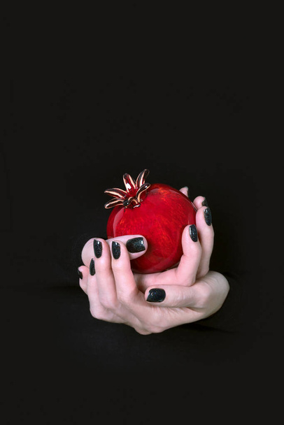 Female hands holding vivid red vase in the shape of a pomegranate fruit on a black background, copy space - Zdjęcie, obraz
