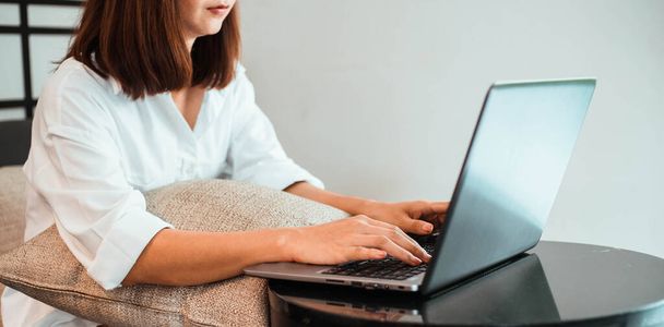 mujer joven que trabaja en el ordenador portátil mientras está sentada en la sala de estar. trabajo desde el concepto de casa - Foto, Imagen