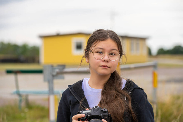 Una giovane preadolescente scatta foto con una fotocamera DSLR. Guarda dritto nella telecamera. Sfondo sfocato e morbido - Foto, immagini