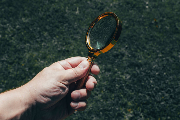 A magnifying glass with a lens in a yellow metal frame in the man's hand - Photo, Image
