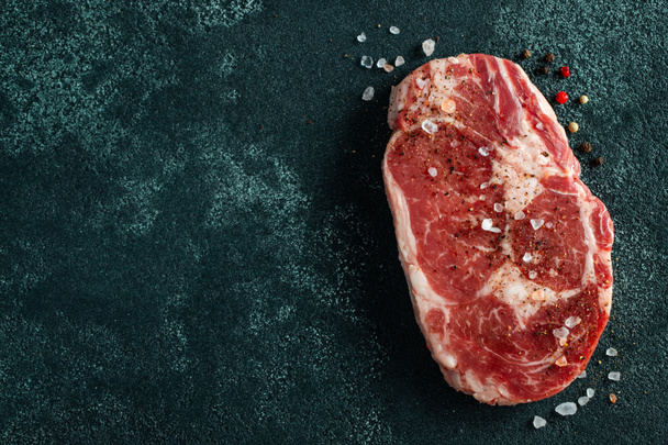 Nyers friss hús Ribeye Steak és fűszerezés sötét háttérrel. Felülnézet fénymásoló felülettel. Lapos fektetés. - Fotó, kép