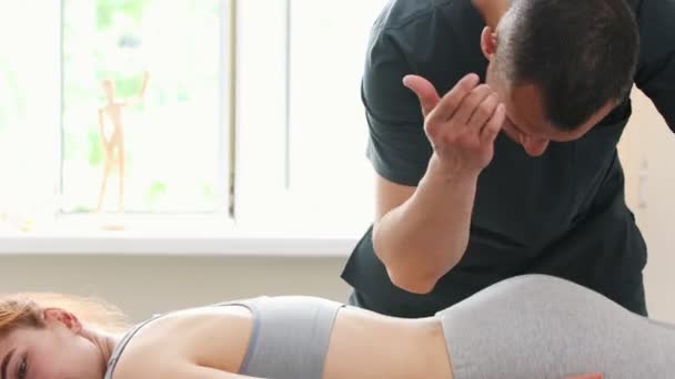 Junge Frau bei der Massage - auf einer Couch liegend - der Massagetechniker drückt mit seinem Ellbogen auf ihr Lendenbein - Filmmaterial, Video