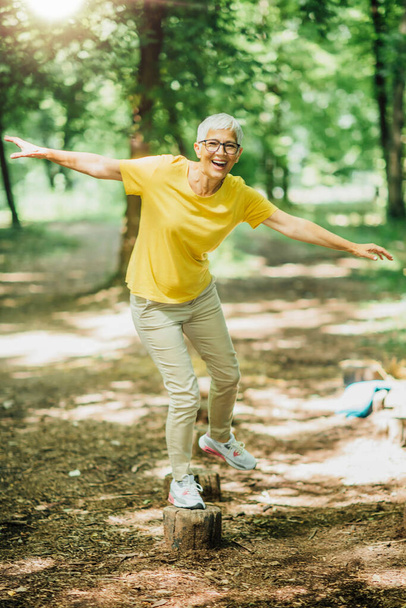 Equilibrar el ejercicio al aire libre. Mujer madura de pie sobre una pierna, ejercitando el equilibrio
  - Foto, imagen
