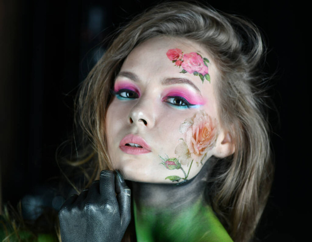 belle fille avec des fleurs sur son visage et peint avec des pivoines bordeaux posant dans différentes poses sur un fond noir - Photo, image