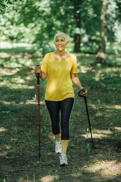 Ćwiczenia nordic walking. aktywny Dojrzałe kobieta cieszy się w natura - Zdjęcie, obraz