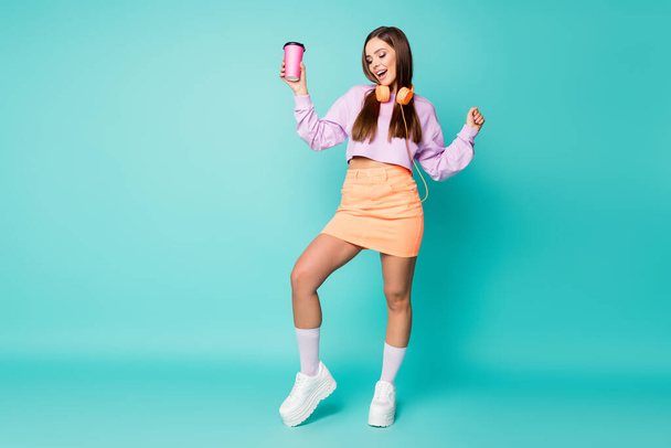 Full body photo of attractive lady hold coffee mug listen modern technology earphones dance tender moves wear violet sweater orange skirt shoes socks isolated teal color background - Фото, зображення