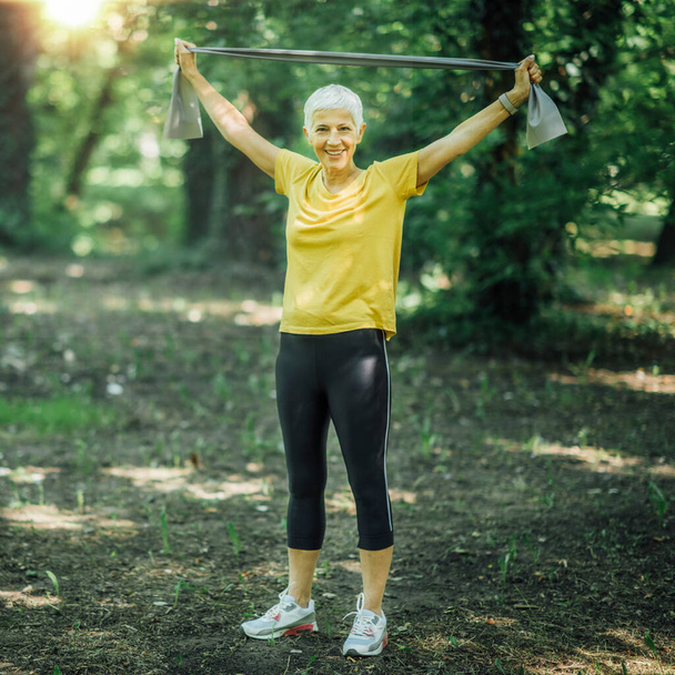 Direniş bandı yürüme egzersizi. Olgun bir kadın elastik direniş bandıyla güç çalışması yapıyor.  - Fotoğraf, Görsel