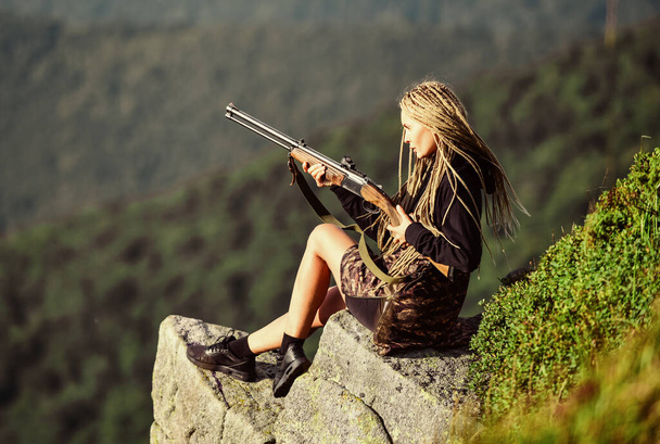 Hunting season. Hunter mountains landscape background. Sexy warrior. Woman attractive long hair pretty face hold rifle for hunting. Amazon girl sit on cliff prepare gun for hunting. Aiming concept - Fotografie, Obrázek