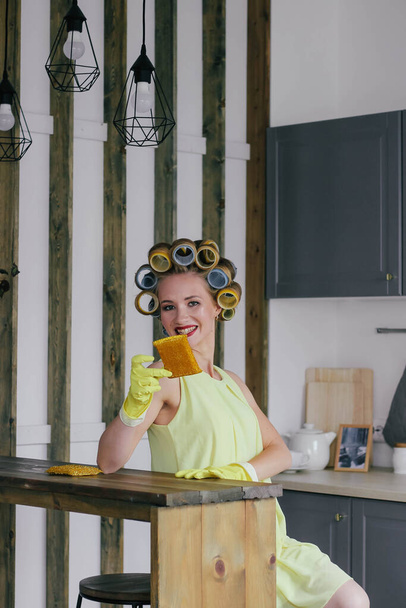 The girl the blonde in curlers and in a yellow dress cleans up with gloves and a sponge - Photo, Image