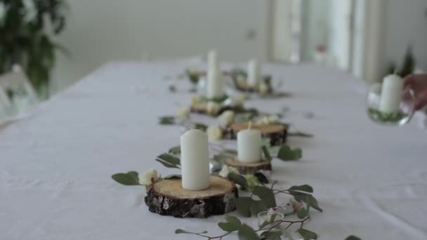 Feestelijke vormgeving van de trouwtafel. Een vrouw plaatst glazen vazen met kaarsen op houten cirkels tussen de bloemen. Close-up - Video