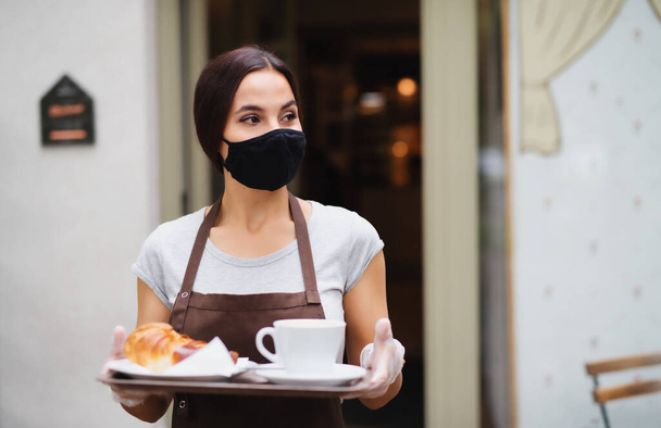 Официантка в маске работает в кафе, обслуживает клиентов
. - Фото, изображение