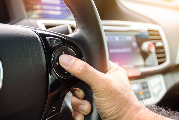 Водитель нажимает кнопку громкости автомобильного радио на руле автомобиля - Фото, изображение