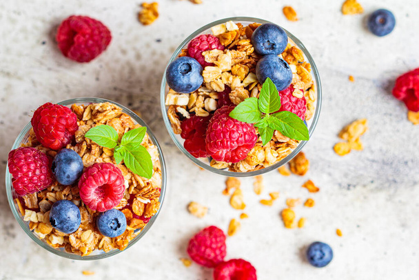 Yogurt parfait with granola, raspberries and blueberries in glasses, light background. Healthy breakfast concept. - Foto, Imagem