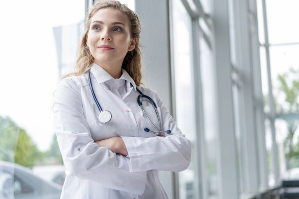 Portrait of young woman doctor with white coat standing in hospital. - 写真・画像