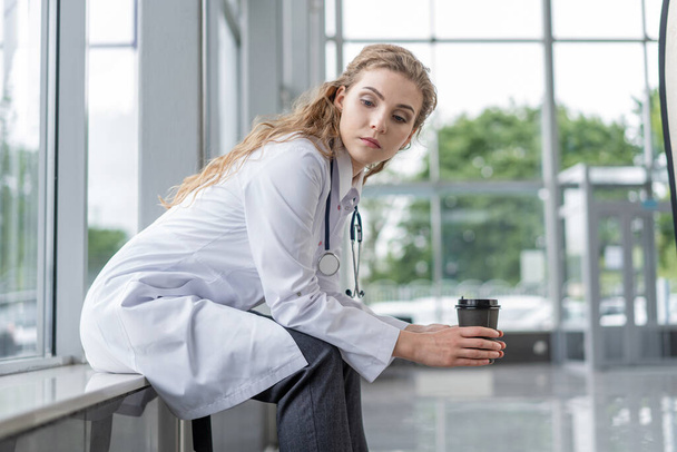 Portrait of tired exhausted nurse or doctor having a coffee break in hospital. COVID-19, Coronavirus pandemic. - Foto, Imagen