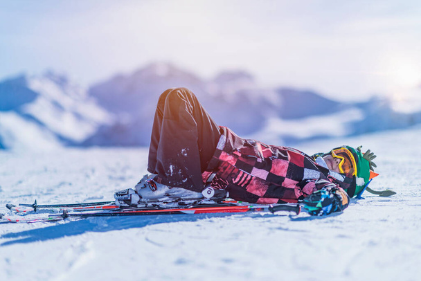Мальчик лежит на снегу, отдыхает на вершине горнолыжного курорта
. - Фото, изображение