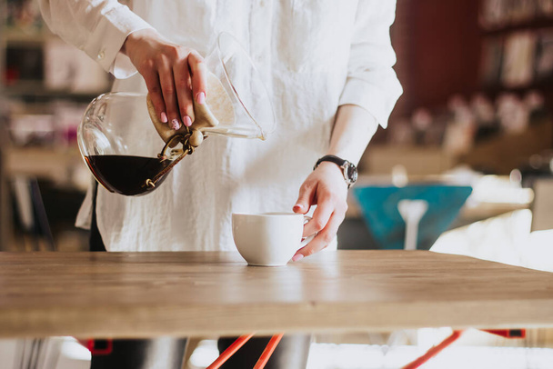 A girl in a white shirt pours coffee into the porridge. Chemex. Alternative ways of brewing coffee. Coffee shop concept - Zdjęcie, obraz
