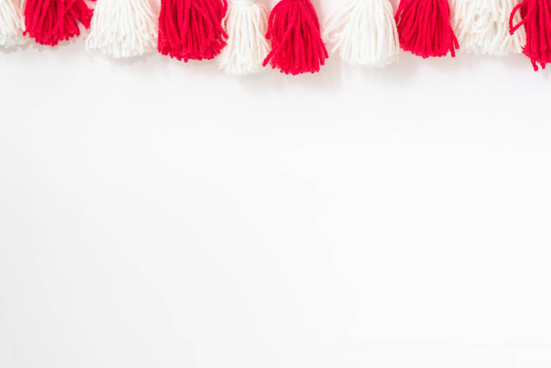 brushes from yarn of red and white color on a white background. Space for copy space. DIY yarn brushes. Garland. Garland of yarn. Pampushki from yarn. Children's creativity - Фото, изображение