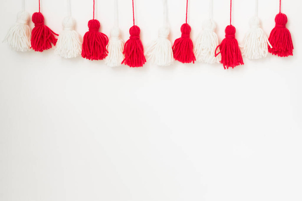 brushes from yarn of red and white color on a white background. Space for copy space. DIY yarn brushes. Garland. Garland of yarn. Pampushki from yarn. Children's creativity - Foto, imagen